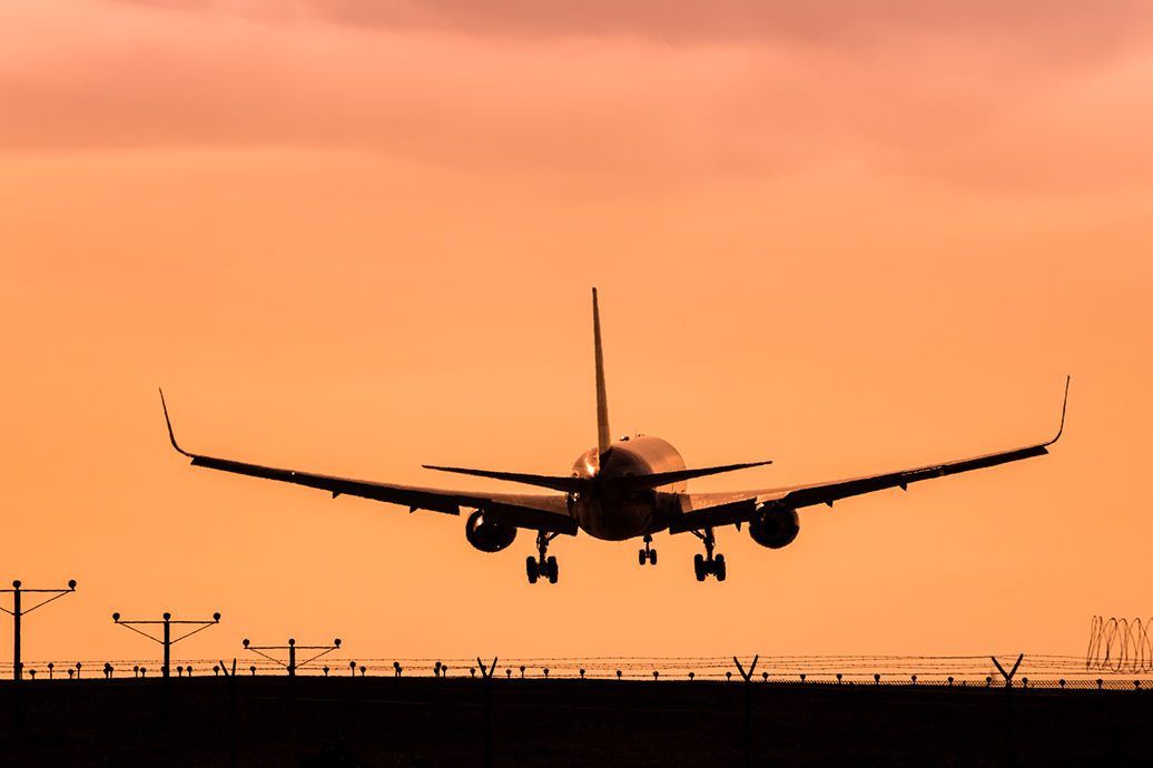 AN airplane taking off under an orange sky.