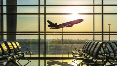 Airplane taking off outside an airport's departure lounge.