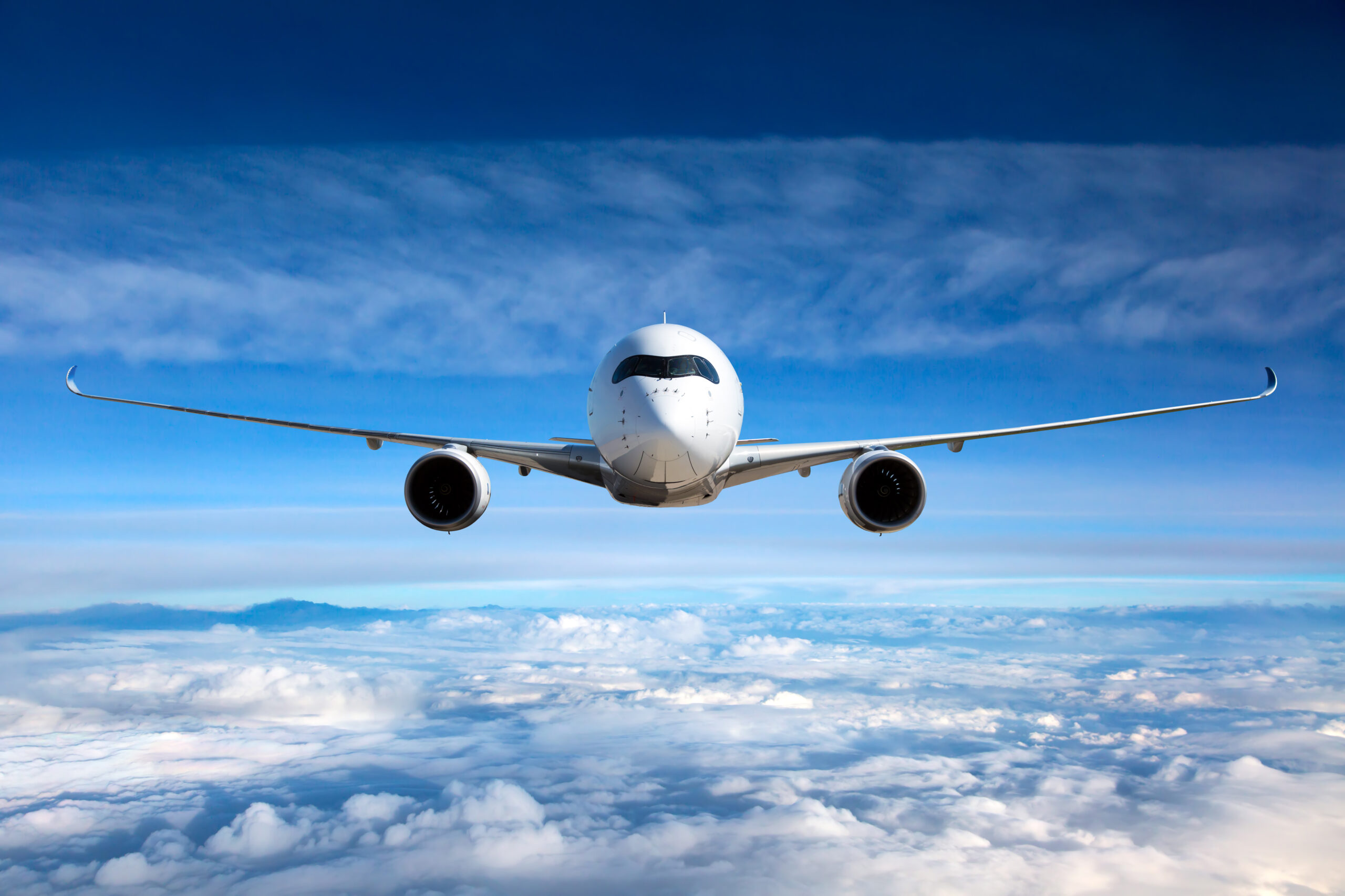 Front view of a commercial airplane flying above the clouds.