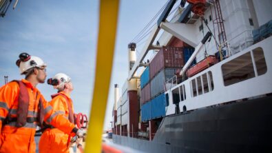 A pair of tug workers stare up at a docked container ship.