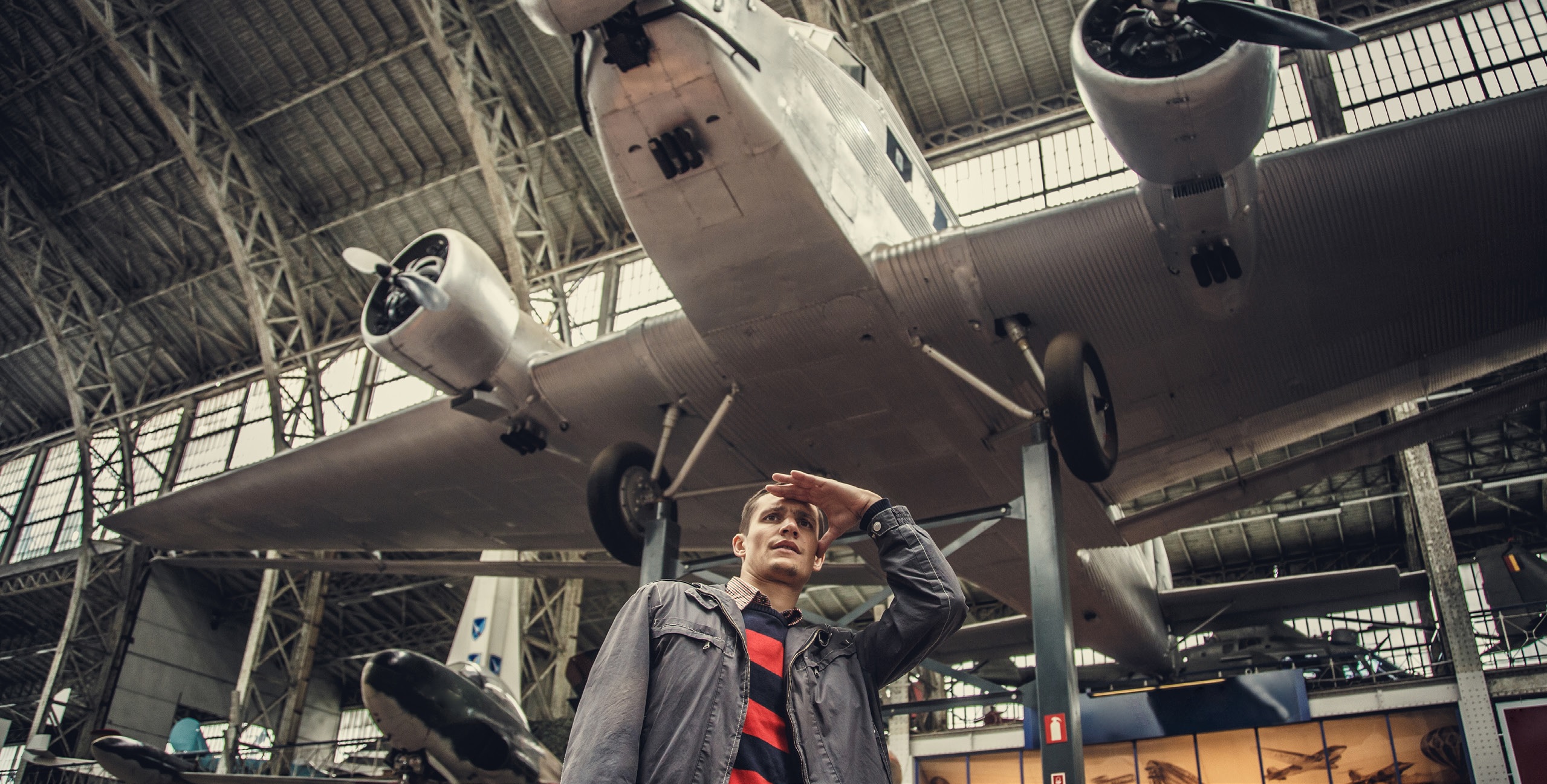 A man standing beneath an old plane suspended in a museum.