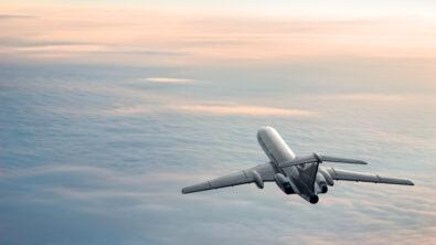 A passenger plane flying over clouds as the sun rises.