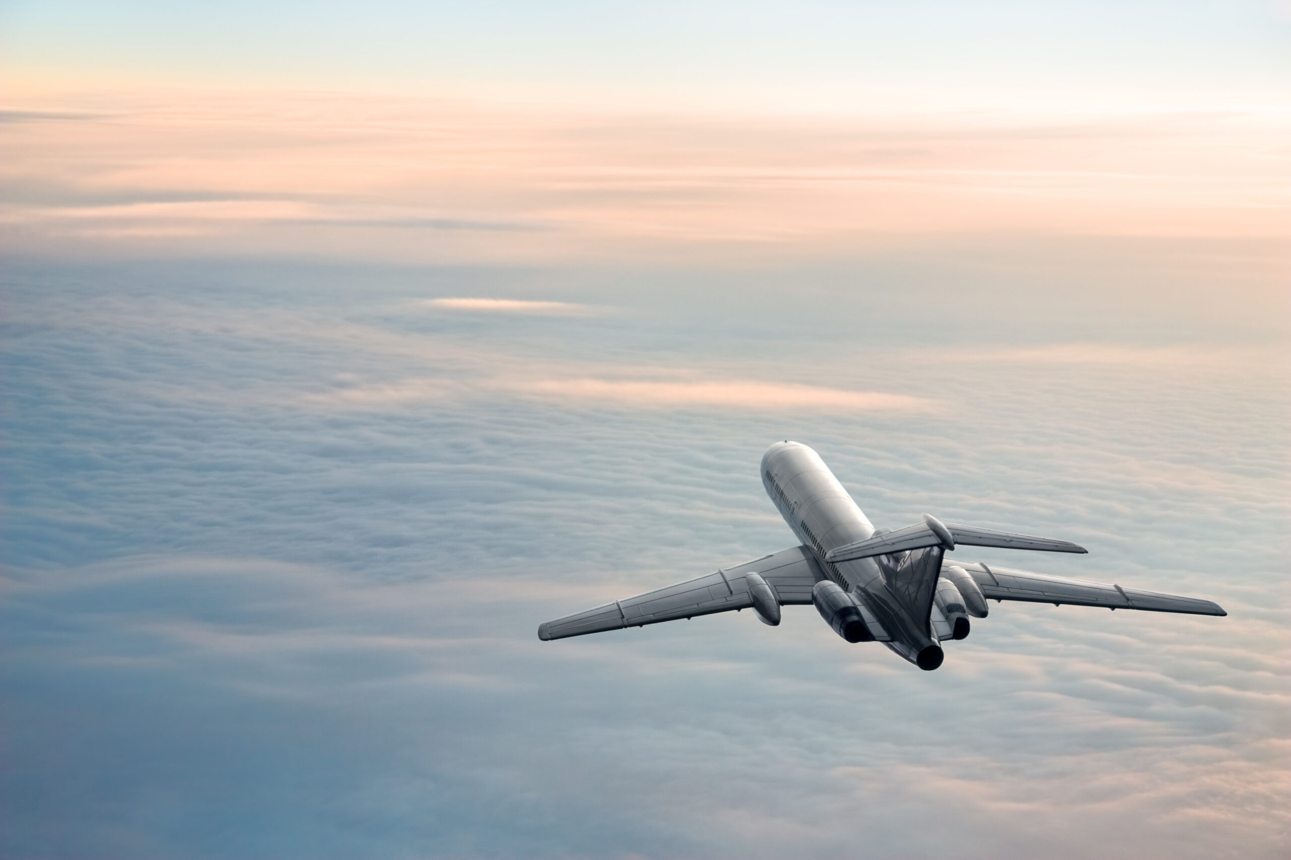 A passenger plane flying over clouds as the sun rises.