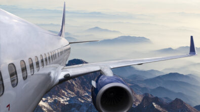 The body and wing of an airplane flying above a mountainous landscape.