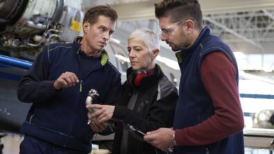 Three aircraft engineers discussing over and electronic tablet in a hangar.