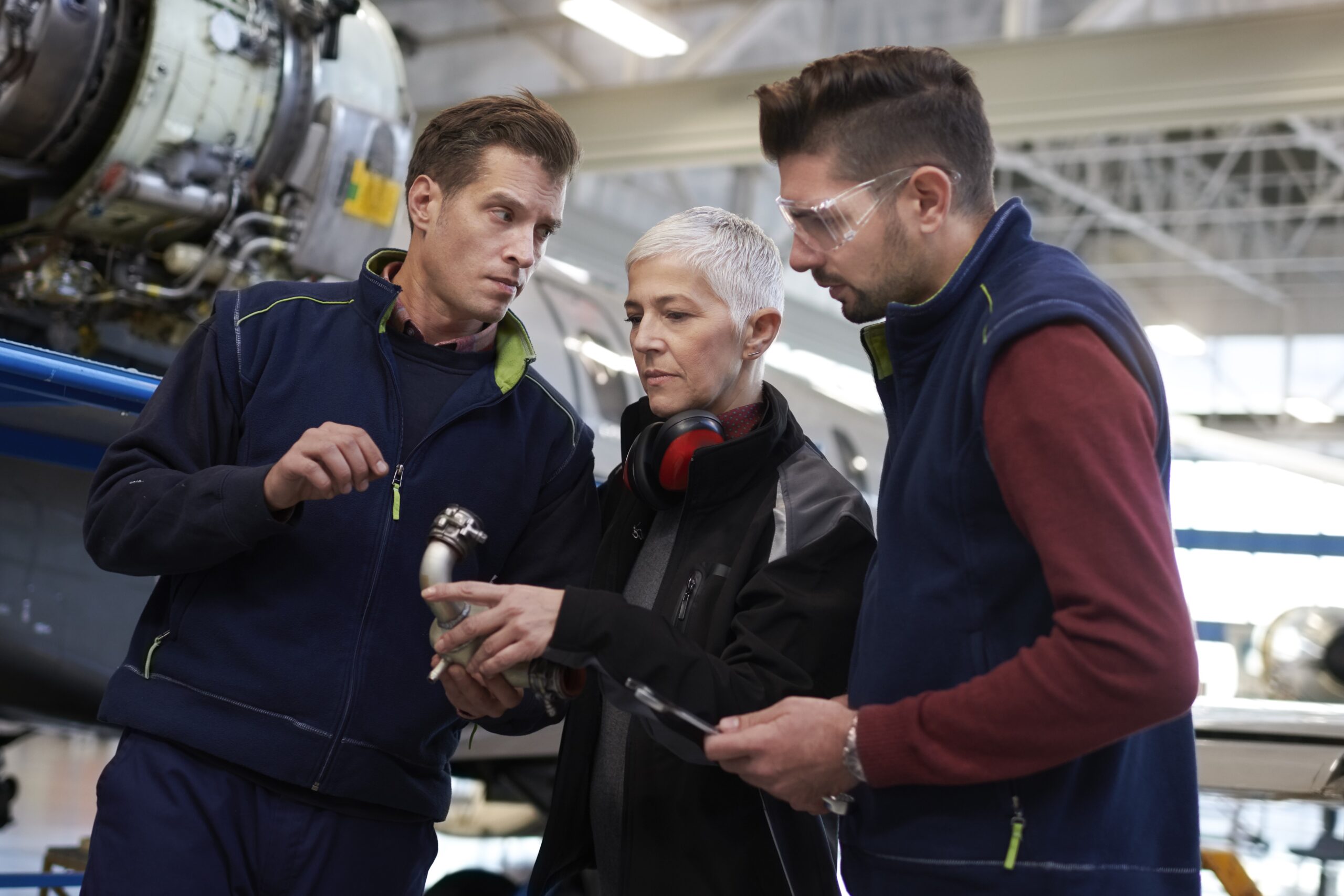 Three aircraft engineers discussing over and electronic tablet in a hangar.