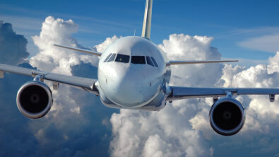 Front view of a commercial aircraft flying in front of a cloud-filled sky.