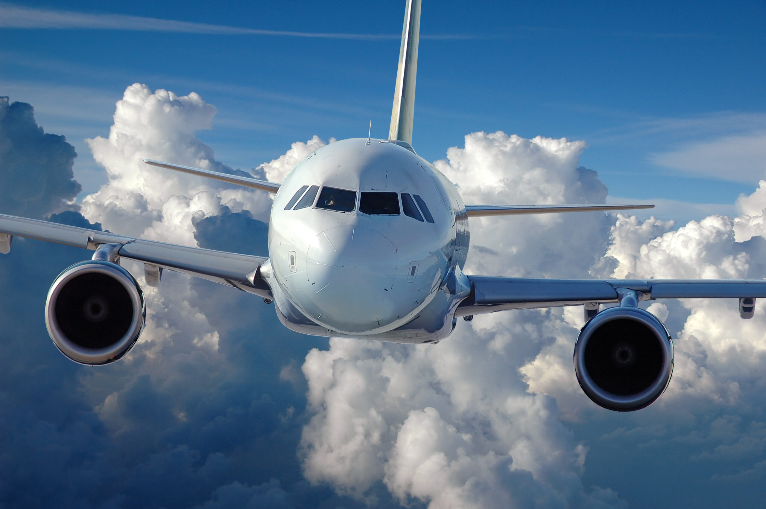 Front view of a commercial aircraft flying in front of a cloud-filled sky.