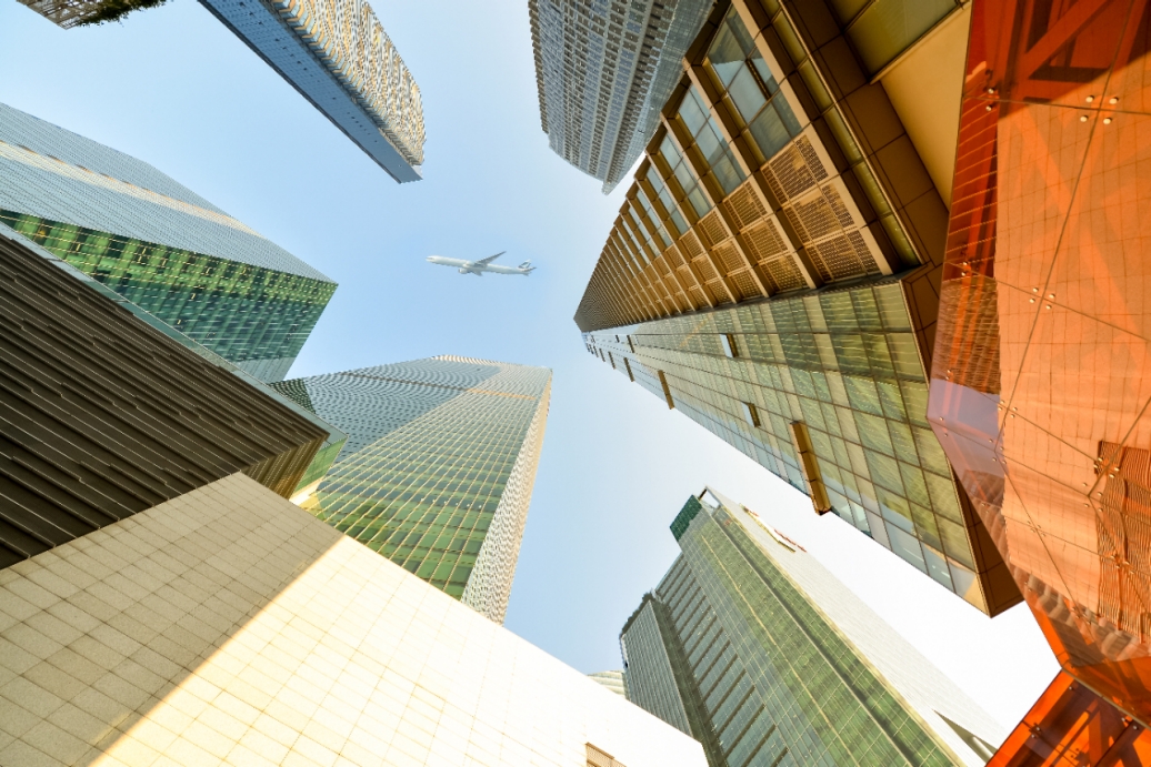 An airplane flying high above skyscrapers from street view.