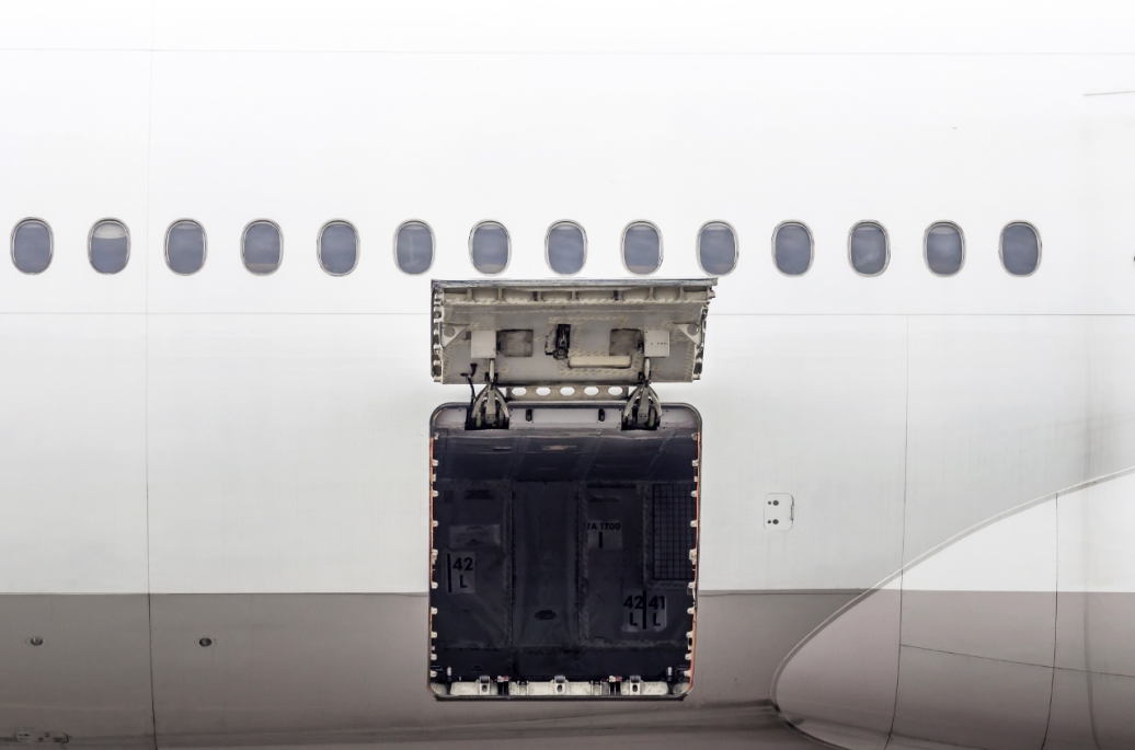 The side of a passenger airplane with the luggage compartment door open.