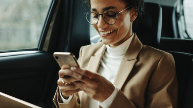 Smiling woman traveling by a car. Businesswoman sitting on backseat of a car and reading text message.