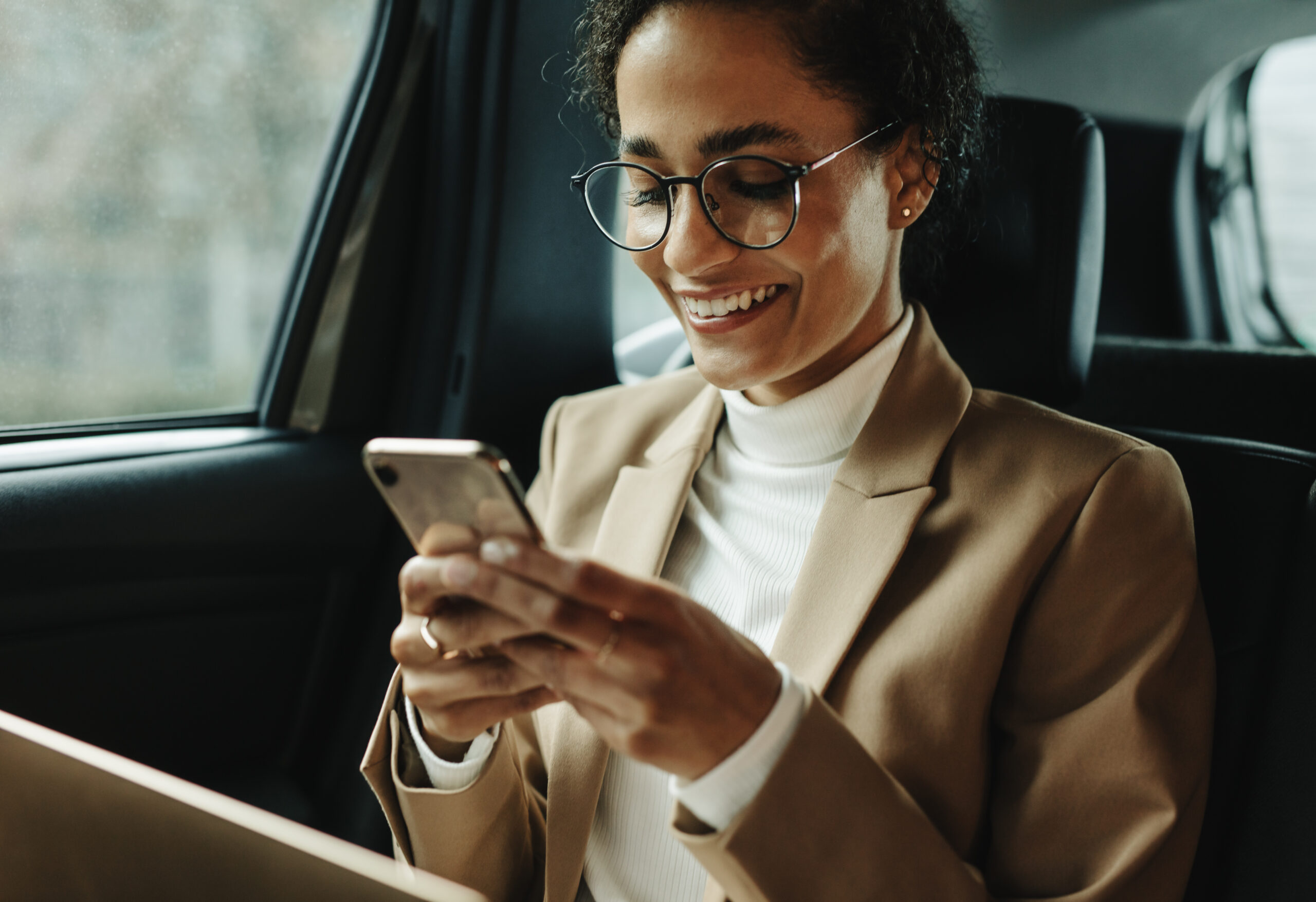 Smiling woman traveling by a car. Businesswoman sitting on backseat of a car and reading text message.