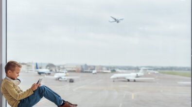 young boy sitting inside airport terminal in the window playing a video game