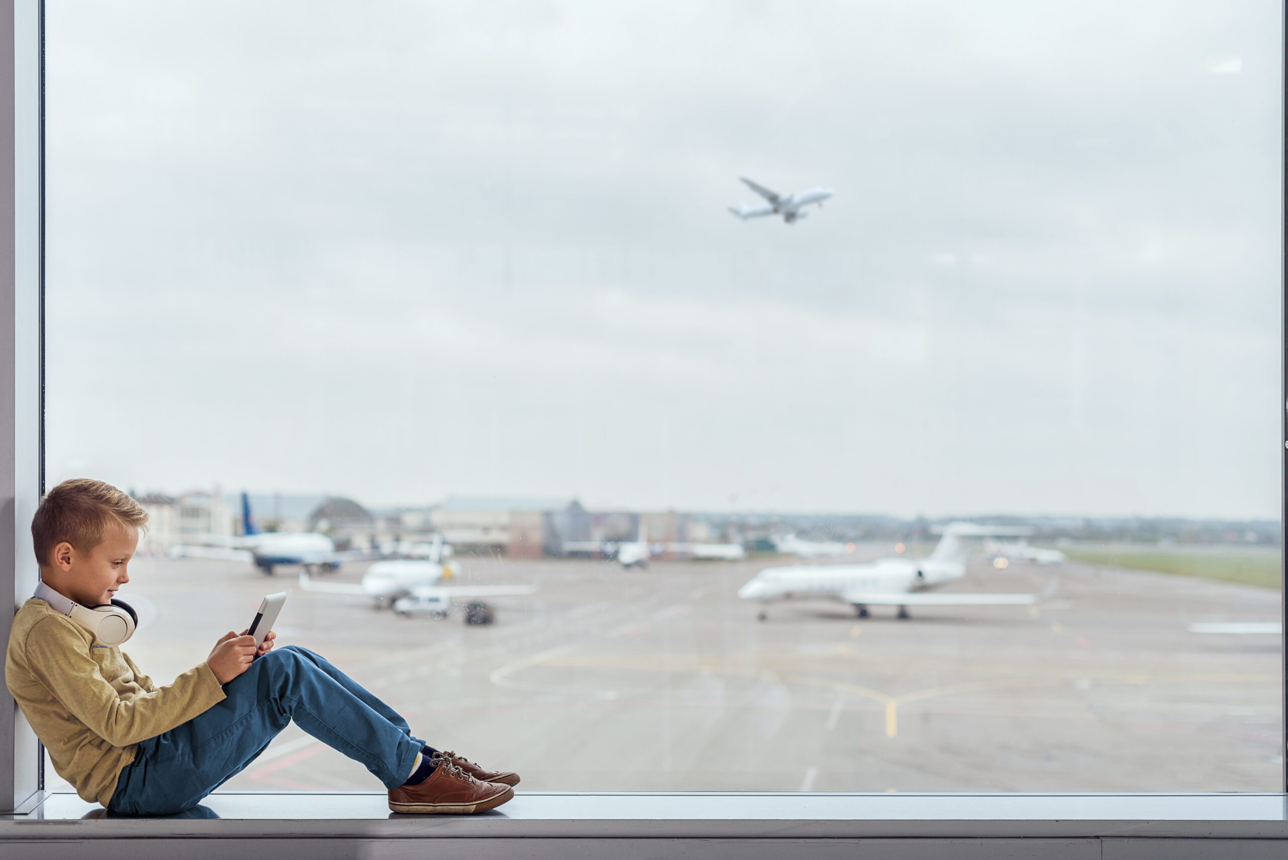 young boy sitting inside airport terminal in the window playing a video game