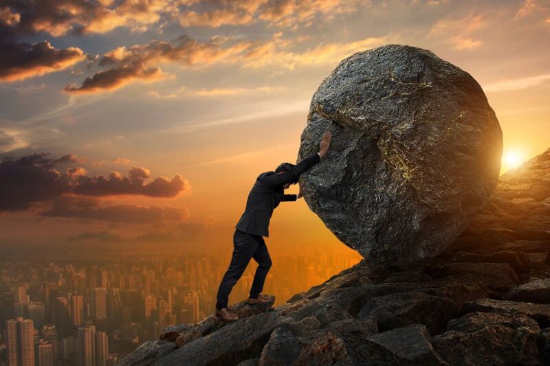 man pushing boulder uphill at sunrise