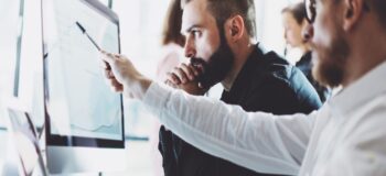 two men looking at a computer screen evaluating scheduling and planning