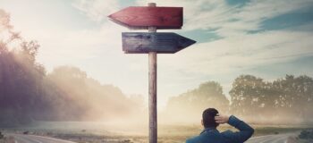 Businessman in front of crossroad and signpost arrows shows two different courses, left and right direction to choose. Road splits in distinct direction ways.