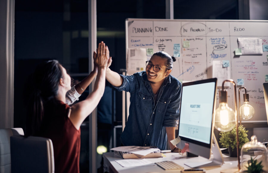 A man and woman in a modern office setting high five in celebration of an achievement. S&T partners can work with traditional channel partners to win more deals.