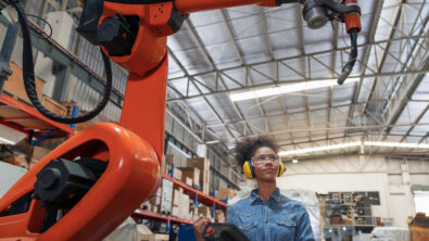 Siemens Teamcenter is part of Microsoft Cloud for Manufacturing. In this photo, a robot controls manufacturing operations while an employee looks on.