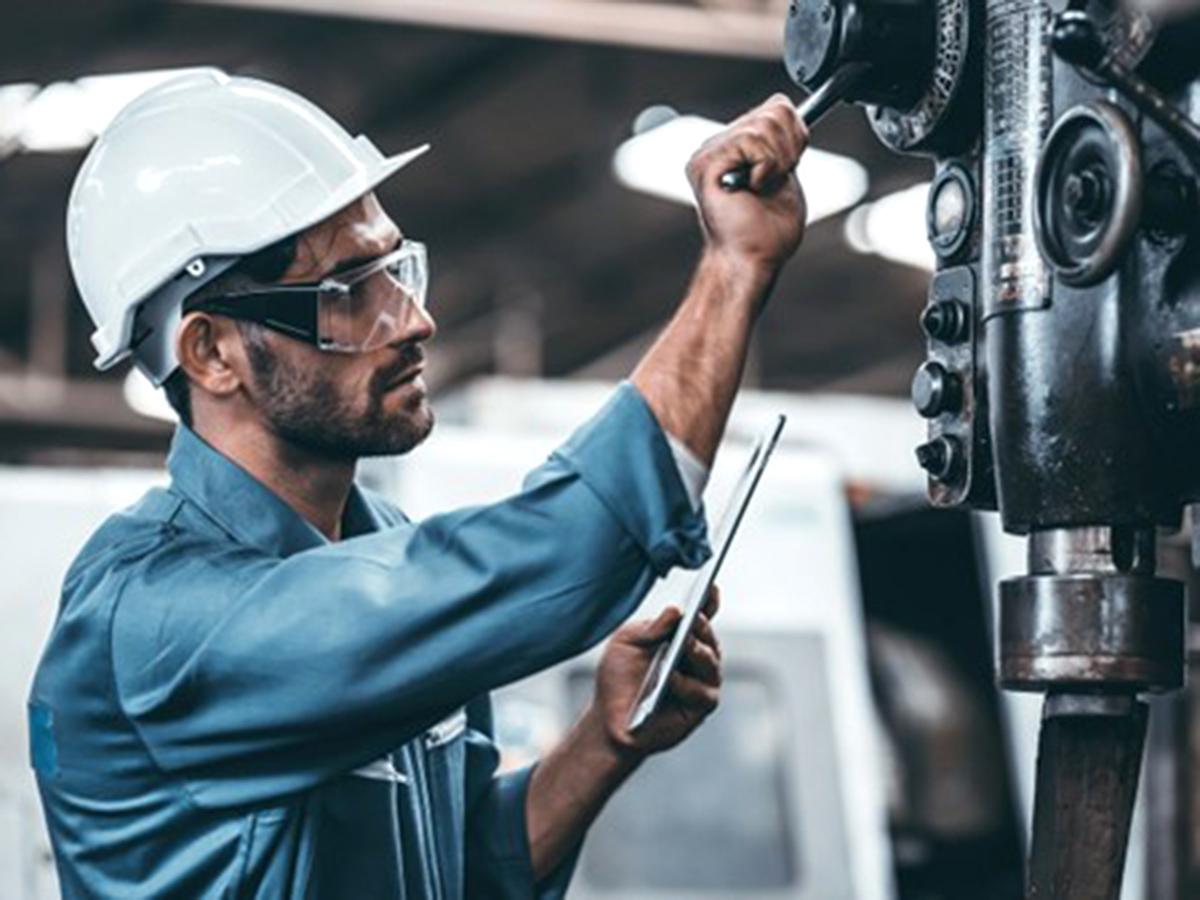 A factory worker consults a tablet computer while working on a machine. The ability for apps built using low-code platforms enables servitization in the manufacturing vertical.