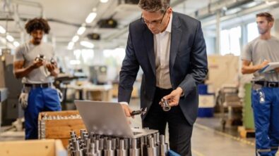 A man wearing a suit in a factory looks at laptop screen, highlighting the need for customized PLM solutions.