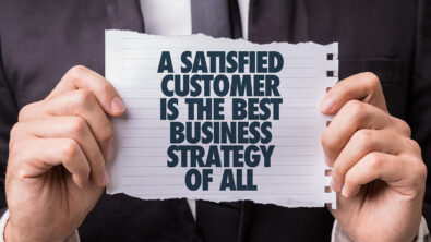 A man holds a small piece of paper that has the words "A satisfied customer is the best business strategy of all" printed on it.