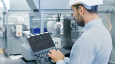 Engineer reviewing manufacturing performance data on a laptop screen in an electronic PCB manufacturing facility