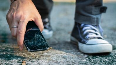 person picking up cell phone with cracked screen from the sidewalk after dropping it