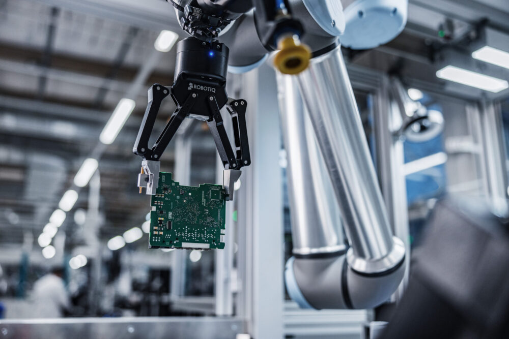 Image of a printed circuit board held by machinery inside an electronics manufacturing plant using intraplant logistics