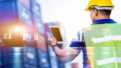 A marine worker holding a tablet with a ship in the background