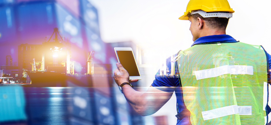 A marine worker holding a tablet with a ship in the background