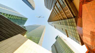 An airplane flying high above skyscrapers from street view.