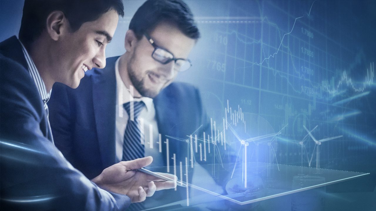 Two engineers collaborating in front of a large tablet with a digital overlay of a wind turbine and digital charts.