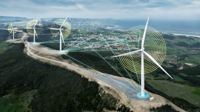 Four wind turbines on hills above city with digital overlay and ocean in background.