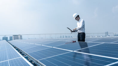 Technician working with laptop next to solar panel.