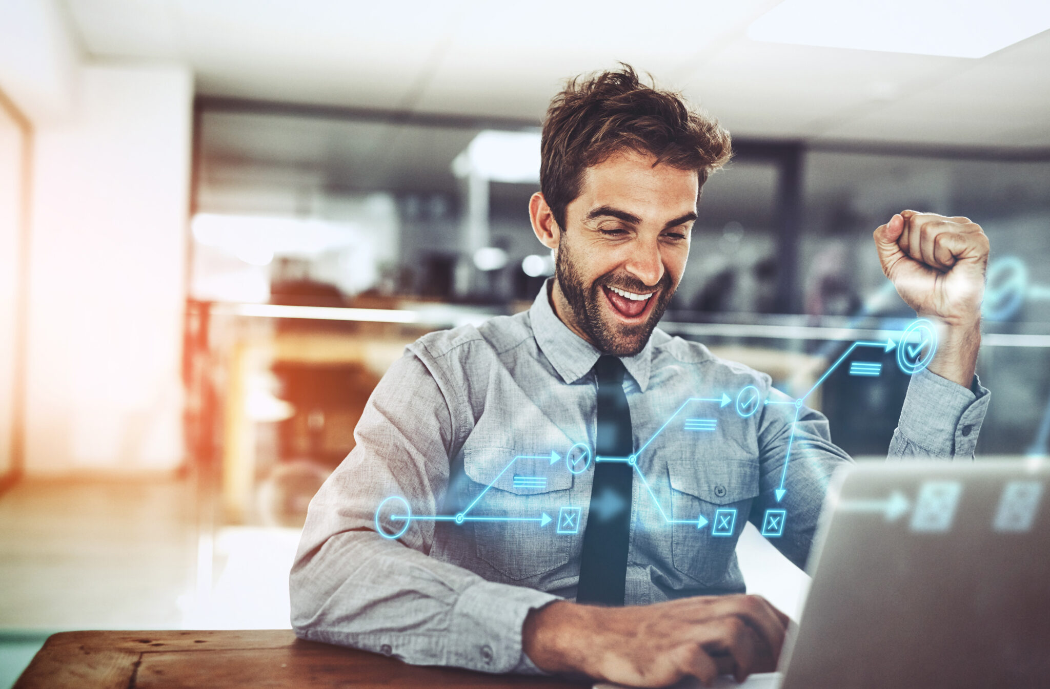 Businessman cheering at his laptop with a fist in the air. There is a digital overlay of a flow chart, representing what is on the computer screen,.