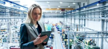 Business woman in manufacturing plant using a tablet, standing in front of heavy machinery