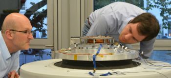 RWTH professors and future engineers examine a satellite piece fitted on a shaker table