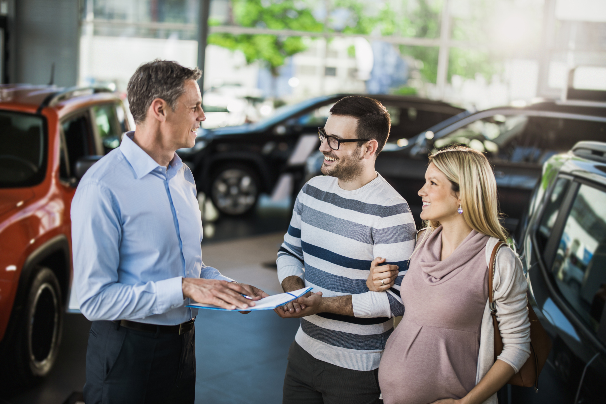 A happy couple talks to a car vendor in a car dealership.