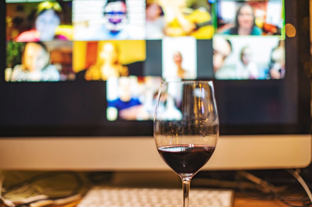 A glass of wine is set in front of a computer displaying a virtual meeting room.