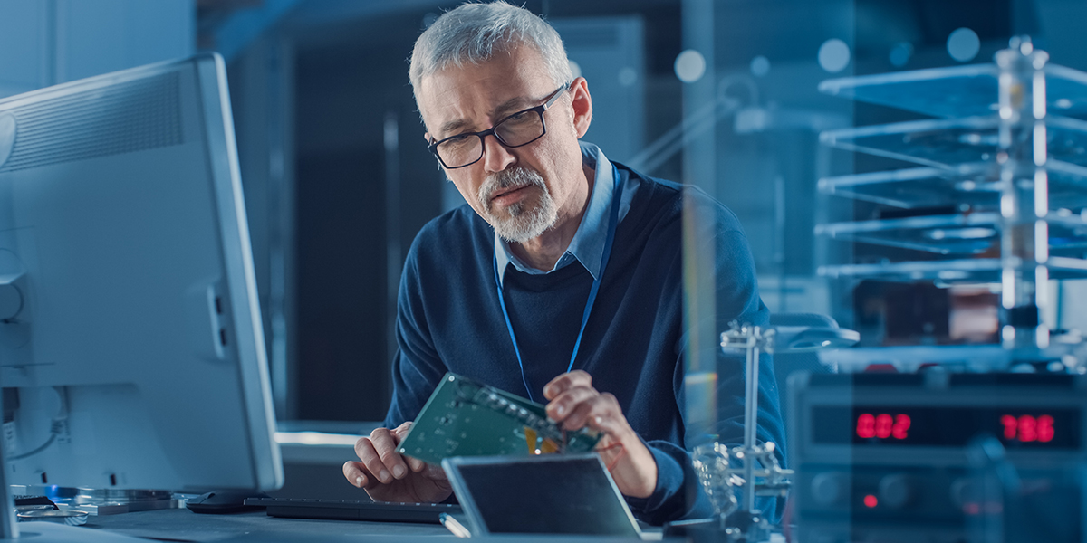 Engineer seated at computer studying physical prototype for early planning of interconnect systems and design verification workflows