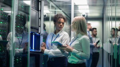 Medium shot of two women working in a data center with rows of server racks and checking the equipment and discussing their work