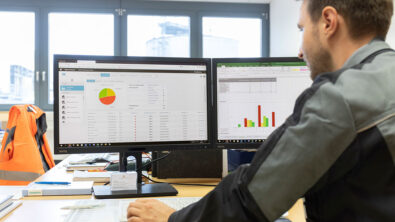 A man looking at two computer screens with charts and graphs displayed on them