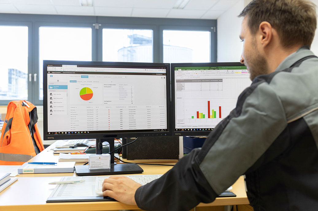 A man looking at two computer screens with charts and graphs displayed on them