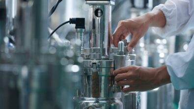 Close up of the hands of a worker in a chemical manufacturing plant. Surrounded by chrome machinery.