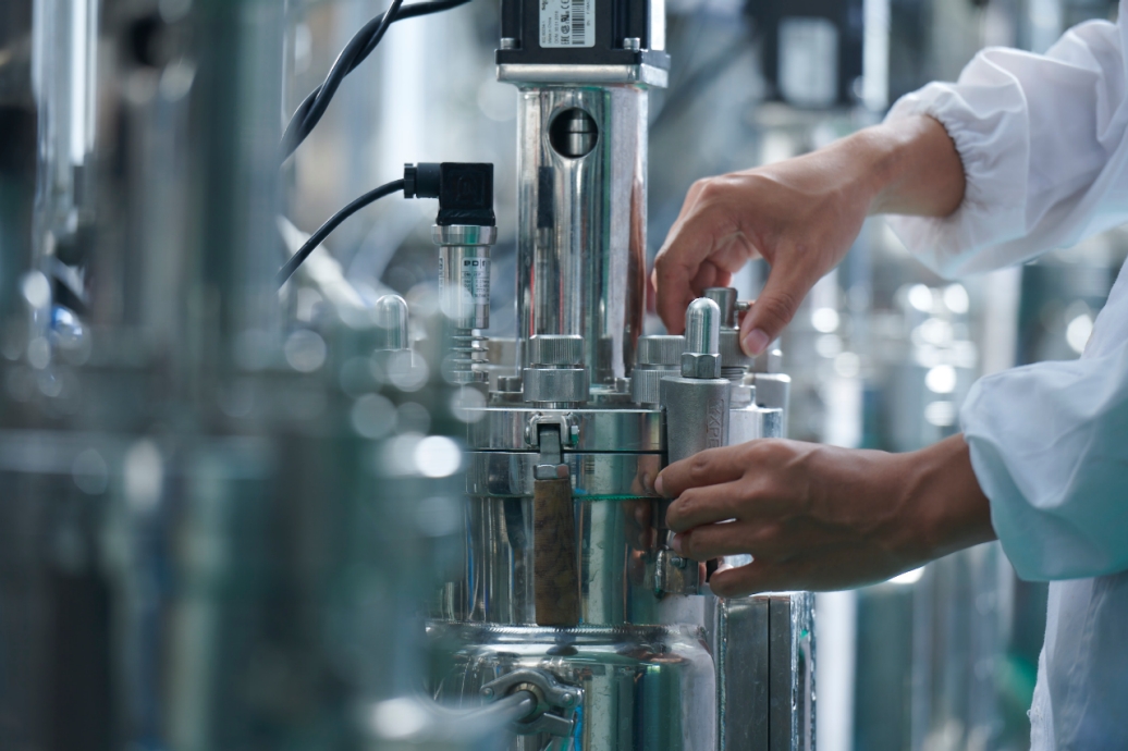 Close up of the hands of a worker in a chemical manufacturing plant. Surrounded by chrome machinery.