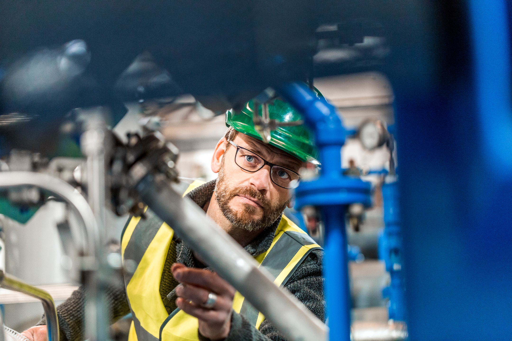 Man wearing green helmet examining a piece of machinery