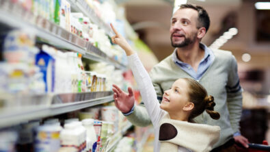 Happy girl pointing at pack of youghurt on upper shelf in supermarket